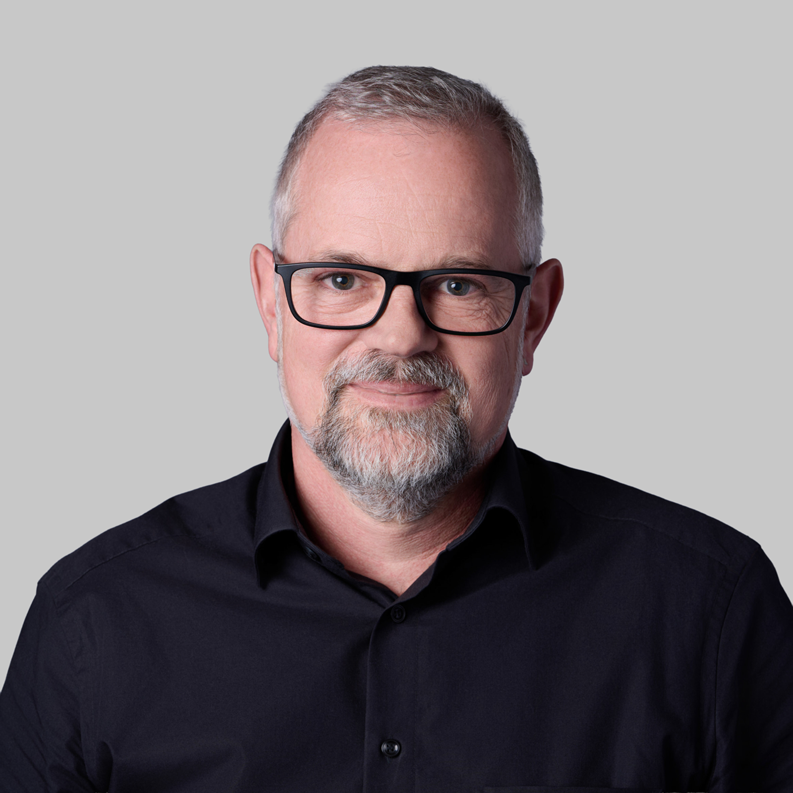 Professional executive headshot of a man with glasses against a grey background