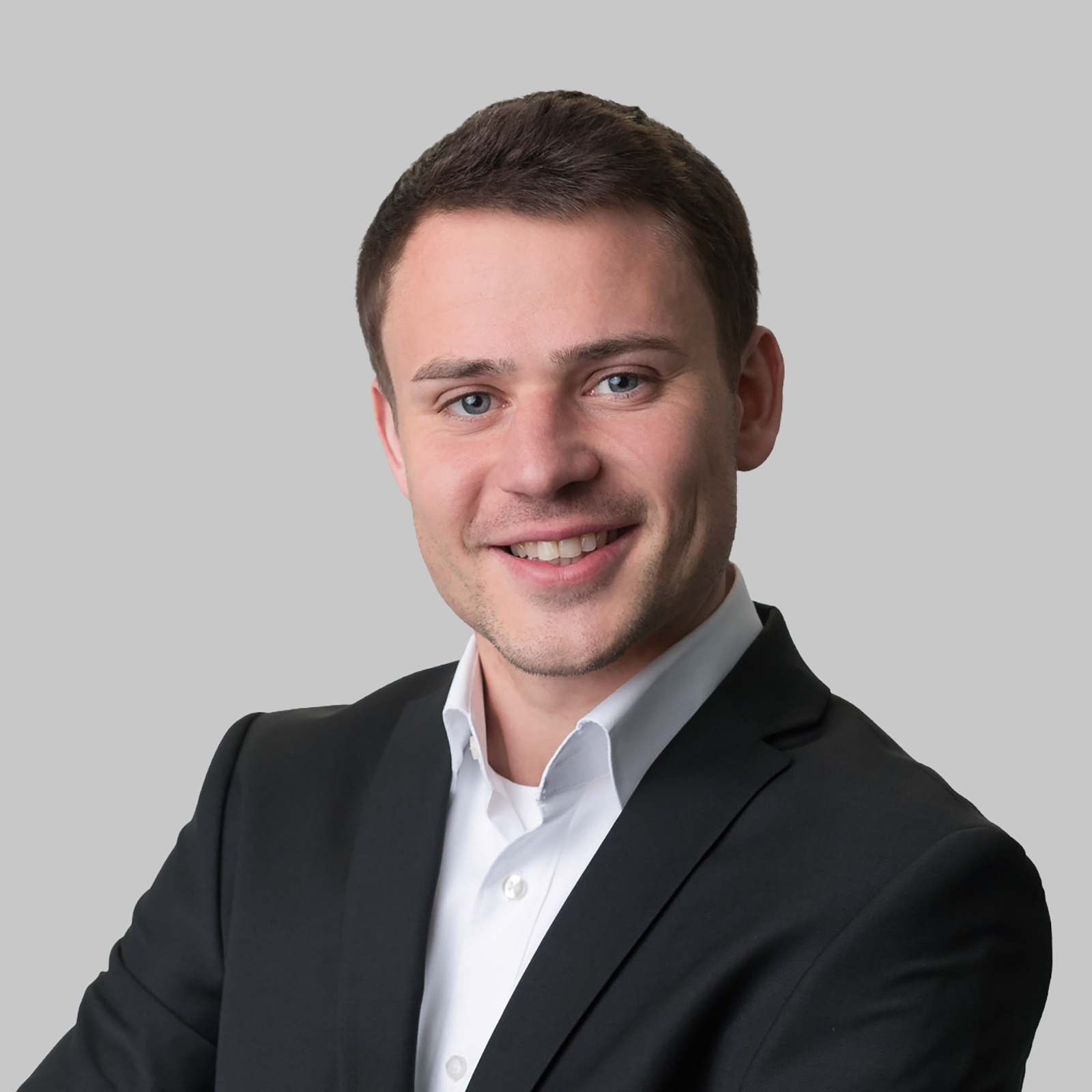 Professional executive headshot of a young man in a dark suit against a grey background